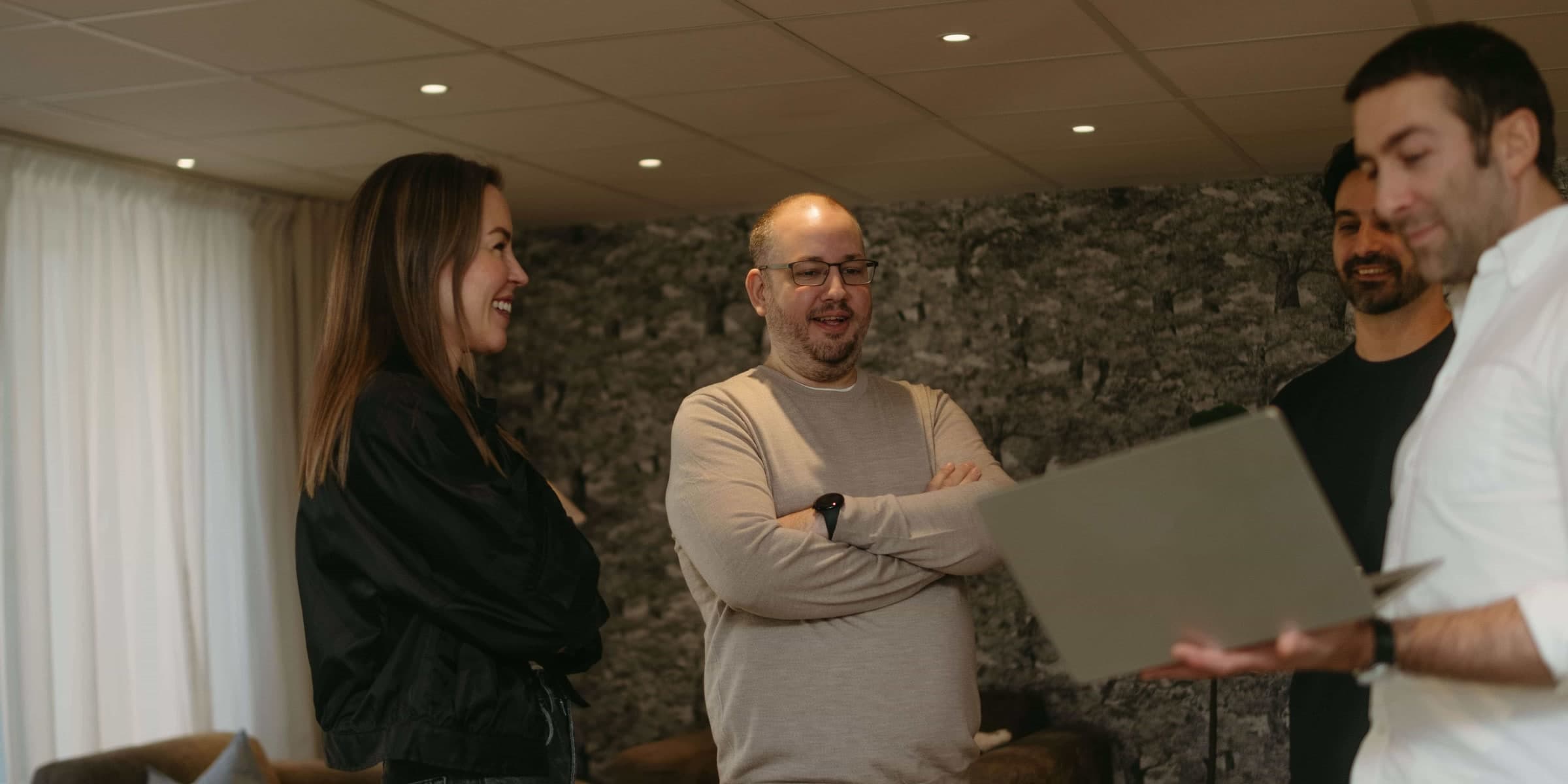 Four of the Engrate team standing and talking in the office, one of them holding an open laptop